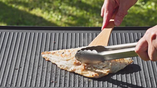 outdoor cooking. cook preparing fresh sea bream fish fillet with spices on hot grill pan for making delicious meal in garden, food closeup, outdoors natural light