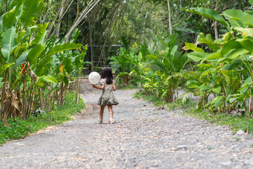 Small Latina girl walks away on gravel zoo path holding a white balloon through tropical foliage.