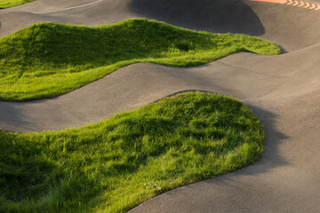 Modern pump track with grass-covered islands, creating abstract wavy landscape in evening light....