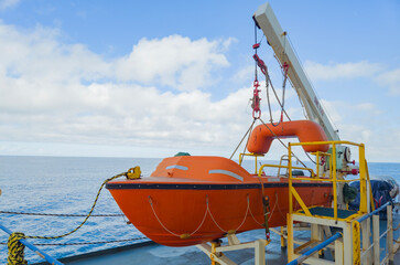 Orange rescue boat secured on a ship deck against a bright blue sky and ocean backdrop. Safety...