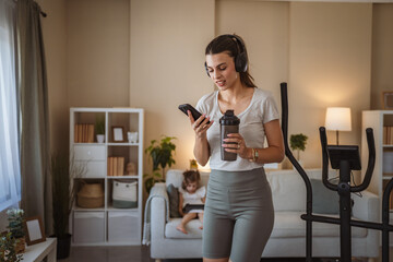 woman with headphones use cellphone and exercise on bike at home