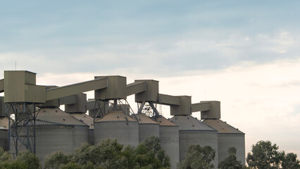 Grain silos against a cloudy sky. Agricultural processing plant with modern architecture. Rural landscape, industrial farming, storage facility