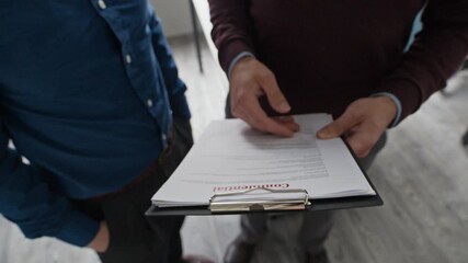 Tilt up and down shot of two focused male colleagues holding clipboard discussing document with confidential corporate information while working collaboratively at modern office - Powered by Adobe
