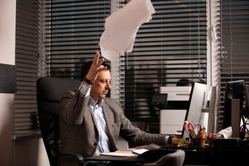 Frustrated businessman throws documents in the air, expressing stress and burnout. Office...