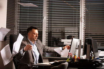 Frustrated businessman throws documents in the air, expressing stress and burnout. Office...