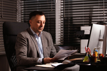 Pensive businessman in a blazer sitting at desk in modern office, staring thoughtfully at computer...