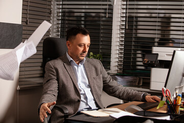Frustrated businessman throws documents in the air, expressing stress and burnout. Office...