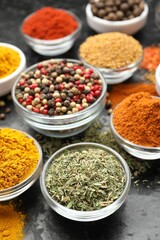 Different aromatic spices in bowls on dark table, closeup