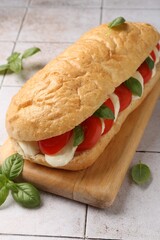 Tasty sandwich with mozzarella cheese, tomatoes and basil on light tiled table, closeup