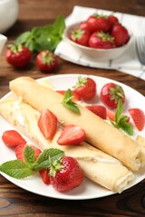 Tasty crepes with cream, strawberries and mint on wooden table, closeup