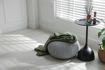 Stylish knitted pouf with plaid and home decor indoors. Space for text