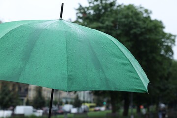 Green umbrella under heavy rain outdoors, closeup