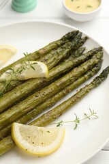 Tasty cooked asparagus served with lemon and thyme on white wooden table, closeup