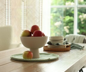 Apples and clean dishware on wooden table in dining room