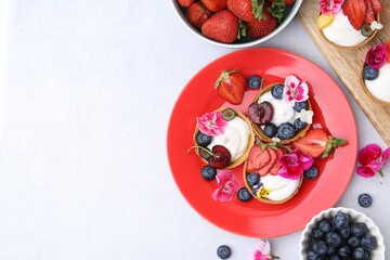 Sweet tartlets with berries and flowers on light grey table, flat lay with space for text....