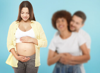 Surrogate mother and intended parents against light blue background, selective focus