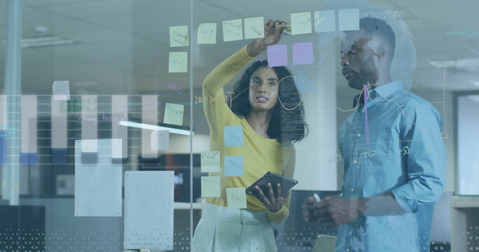 Placing sticky note, brainstorming plan in business attire on glass board in office, with tablet