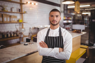 Man in twenties standing behind marble counter with service bell wearing apron at coffee shop