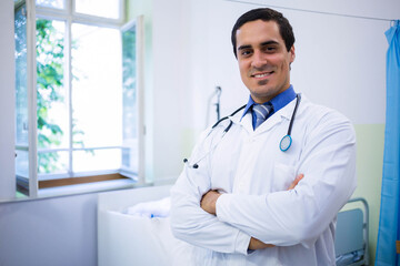 Mid-adult male doctor standing in medical exam room wearing white coat with stethoscope, copy space