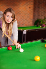 Adult woman leaning over green-felt pool table aiming cue stick at white cue ball at bar