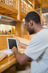 Open textbook lying flat and tablet resting upright under lamp in library study carrel
