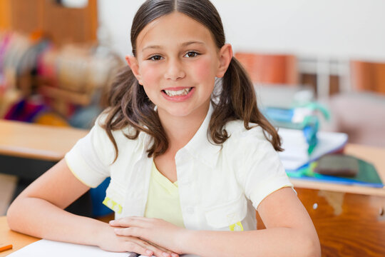 Fototapeta Girl student sitting at wooden desk in classroom smiling with hands folded on notebook and binder