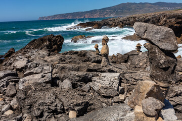 Balanced stone towers on rocky coastal cliffs overlooking the Atlantic Ocean under a clear blue sky...
