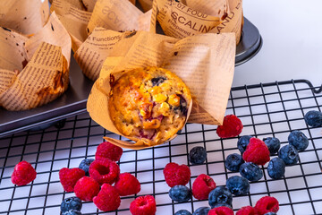 Fruity whole grain muffins with raspberries and blueberries on black tray and white background.
