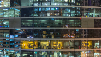 Glowing windows in multistory modern glass and metal office building light up at night timelapse.
