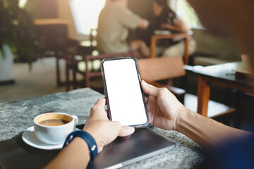 A person holds a smartphone with a blank white screen while sitting in a cafe with a cup of coffee. A versatile mockup for mobile applications.