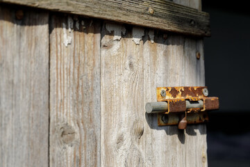A detailed view of a rusty sliding bolt lock attached to an aged, weathered wooden door with...