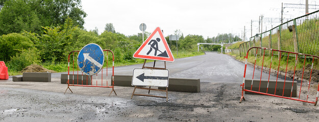 A blocked road under construction with visible traffic signs and barriers indicating a detour and...