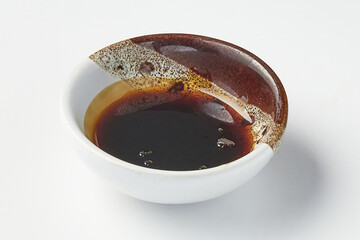 Small ceramic bowl filled with dark, glossy teriyaki sauce, showcasing rich and savory texture, placed on clean white background. bowl has unique, artistic glaze design