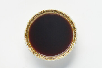 Bowl of dark soy based dipping sauce, commonly used in Japanese cuisine, placed on white background. sauce is rich in color and served in ceramic bowl with textured rim