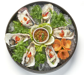 Fresh oysters served on bed of ice with vibrant garnishes, including lime slices, chili, and herbs,...