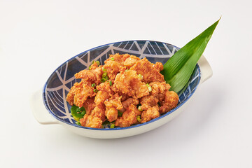 Crispy fried chicken skin served in decorative ceramic bowl garnished with green herbs and banana leaf, showcasing golden brown texture and appetizing appearance