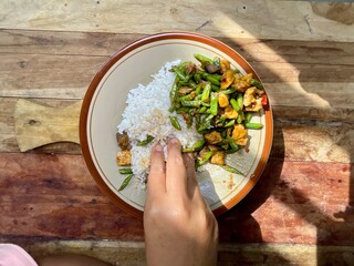 a woman's hand is eating rice, a side dish of stir-fried long beans isolated on ceramic plate on...