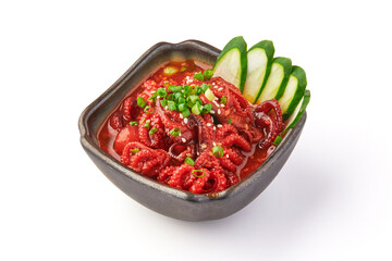 Spicy marinated baby octopus served in black bowl with sliced cucumber garnish, topped with chopped green onions, showcasing vibrant red seasoning and fresh ingredients