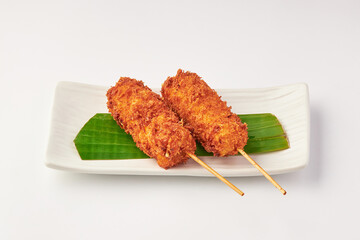 Crispy deep fried cheese sticks on skewers served on rectangular white plate with banana leaf garnish, creating delicious and appetizing presentation
