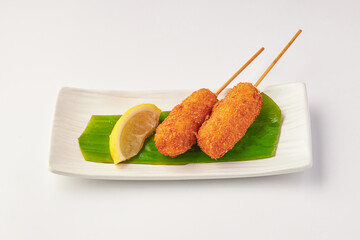 Crispy deep fried cheese sticks served on banana leaf with lemon wedge on rectangular white plate, offering delightful and savory snack option