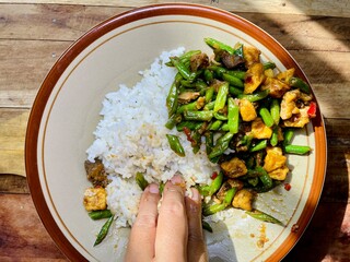 a woman's hand is eating rice, a side dish of stir-fried long beans isolated on ceramic plate on...