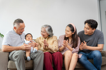 Happy Multi-Generational Asian Family on Sofa at Home, Joyful Grandparents, Parents, and Baby...