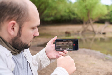Traveler recording a video of a capybara passing by with his smartphone. El Palmar National Park, Entre Rios, Argentina.