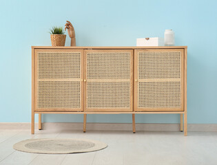 Modern chest of drawers with houseplant and wooden hand near blue wall in room