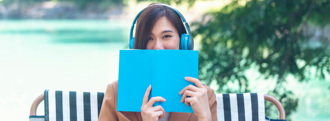 Banner Happy asian woman use headphones listen to music from smartphone outdoor in green park....