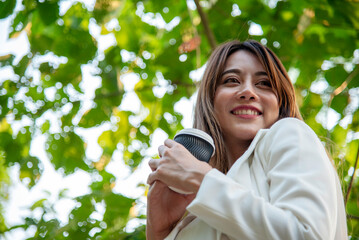 Asian Woman use smartphone drinking coffee hand holding hot disposable cup in green park. Banner...