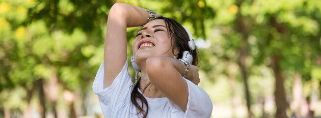 Banner Happy asian woman use headphones listen to music from smartphone outdoor in green park....