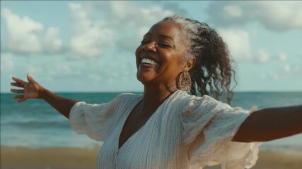 A black woman with joy on her face, arms spread wide, and wind blowing through her hair, standing by the ocean. Sunny day. Happiness and freedom.