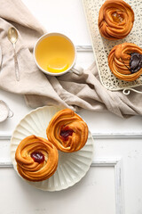Tasty cruffins and cup of tea on white wooden background