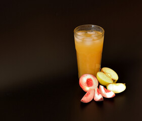 Peach and green apple juice in a tall glass with ice on a black background.